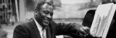 Paul Robeson smiling at piano with sheet music